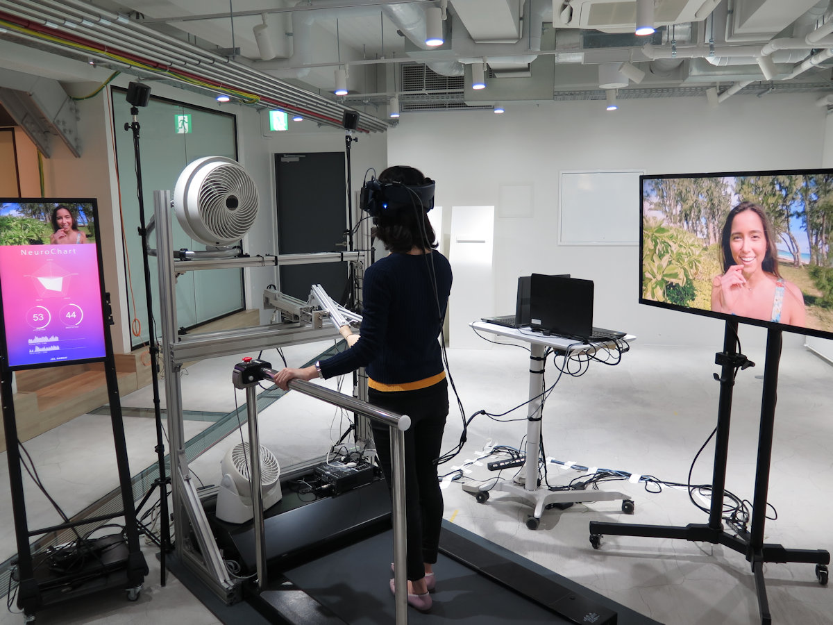 JAL xR Travelerの全景。体験者がVRゴーグルで見ている映像が右端のモニターに映し出されている。モニター内の現地ガイドの女性に手を引かれてハワイの観光地を歩くという設定だ