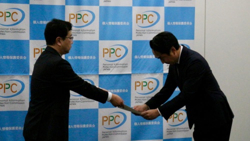 個人情報保護委員会の松元照仁事務局長(左)は2024年3月28日、LINEヤフーの出澤剛社長(右)に勧告文書を手渡した