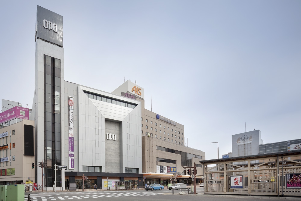  JR秋田駅の駅前広場から見た南側全景。フッ素樹脂塗装したアルミ板でコの字に囲まれた内側に、高さ6層分のコンクリート打ち放しの耐震壁が立ち上がる。写真左側に見えるエレベーター部分は既存のままだ。1974年完成の建物を、耐震補強を含めて全館リニューアルし、2017年10月28日にオープンした（写真：吉田 誠）