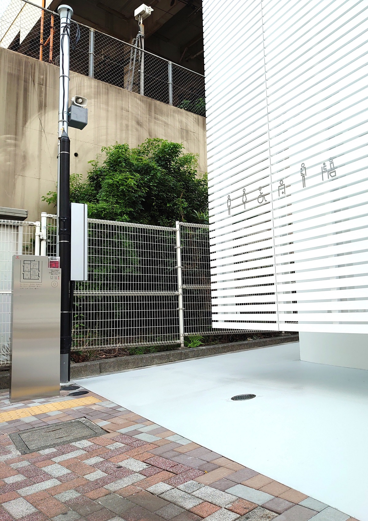 トイレの入り口は、施設の裏手（JRの線路側）にある。アルミルーバーは宙に浮いている。佐藤可士和氏がデザインしたピクトサイン以外は、公衆トイレを思わせるものが歩道からは見当たらない（写真：日経クロステック）