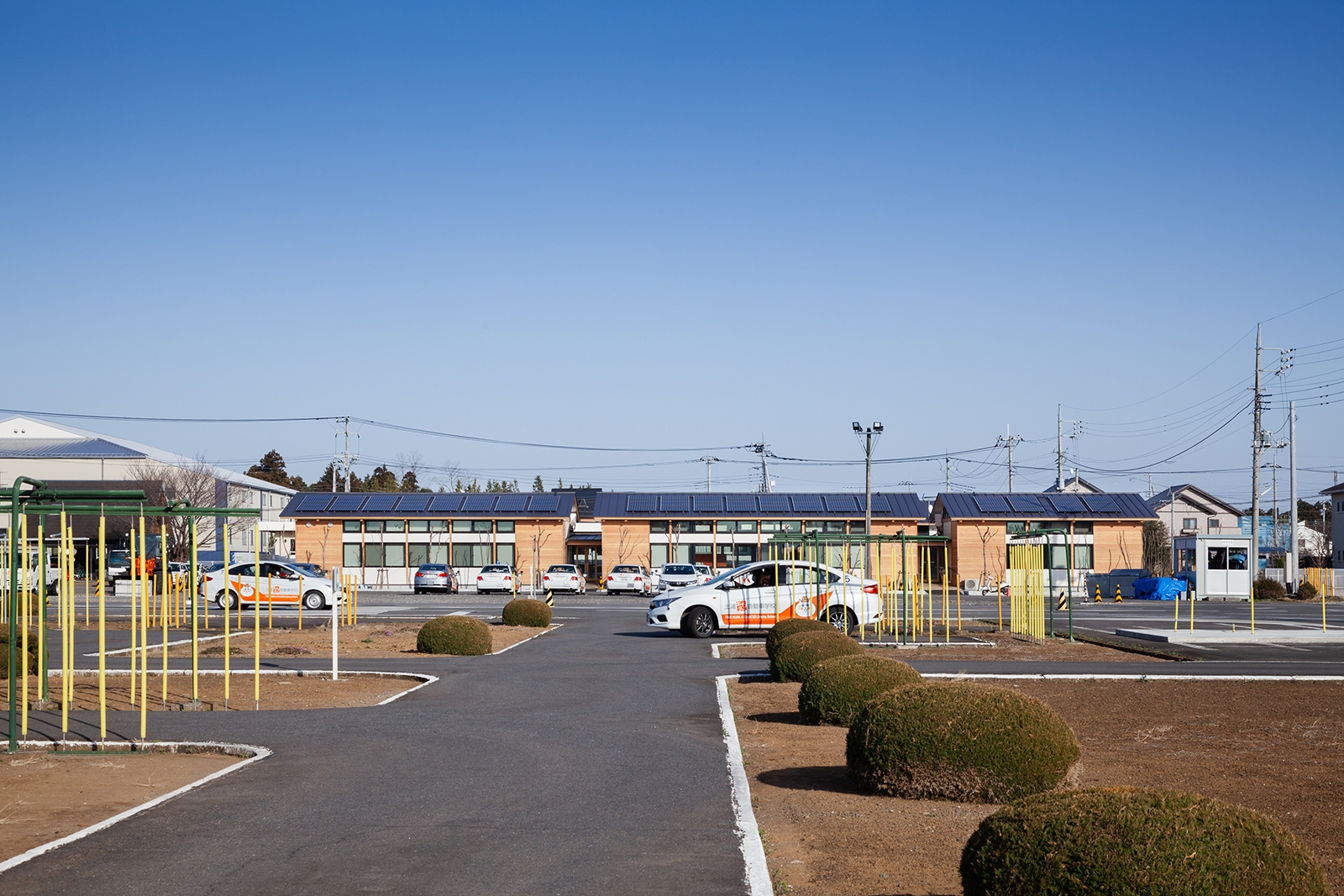  運転練習場越しに見る「土浦北インター自動車学校 校舎棟」の西側外観。手前に並ぶ3棟の屋根上に太陽光発電パネルを載せている（写真：吉田 誠）