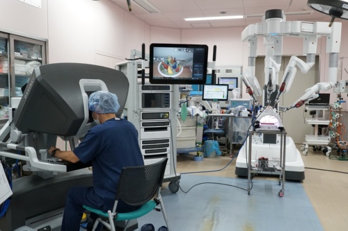 手術支援ロボット「ダビンチ」のシステム。ロボットアーム（右）を遠隔操作する医師（左）。真ん中のモニター画面に、アームが実際に扱っている対象が映し出されている