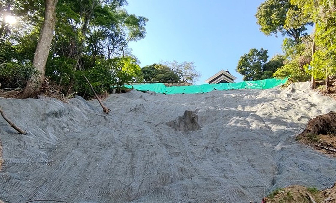 図中の（1）の辺りである斜面上部に侵食防止のため保護シート（写真手前の白っぽい部分）を設置（写真：松山市）