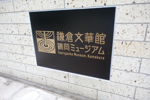 1階の大谷石の壁に張られた「鎌倉文華館 鶴岡ミュージアム」のプレート。左のシンボルマークは、池に立つ柱と波紋をモチーフにした（写真：日経アーキテクチュア）