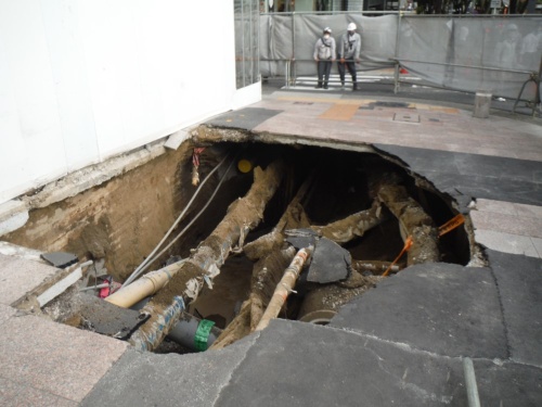 陥没した歩道の様子。埋設管があらわになっている。写真奥に見える灰色の仮囲いは、工事中に出水を確認した竹中工務店が陥没前に緊急対応として設置した(写真:名古屋市)