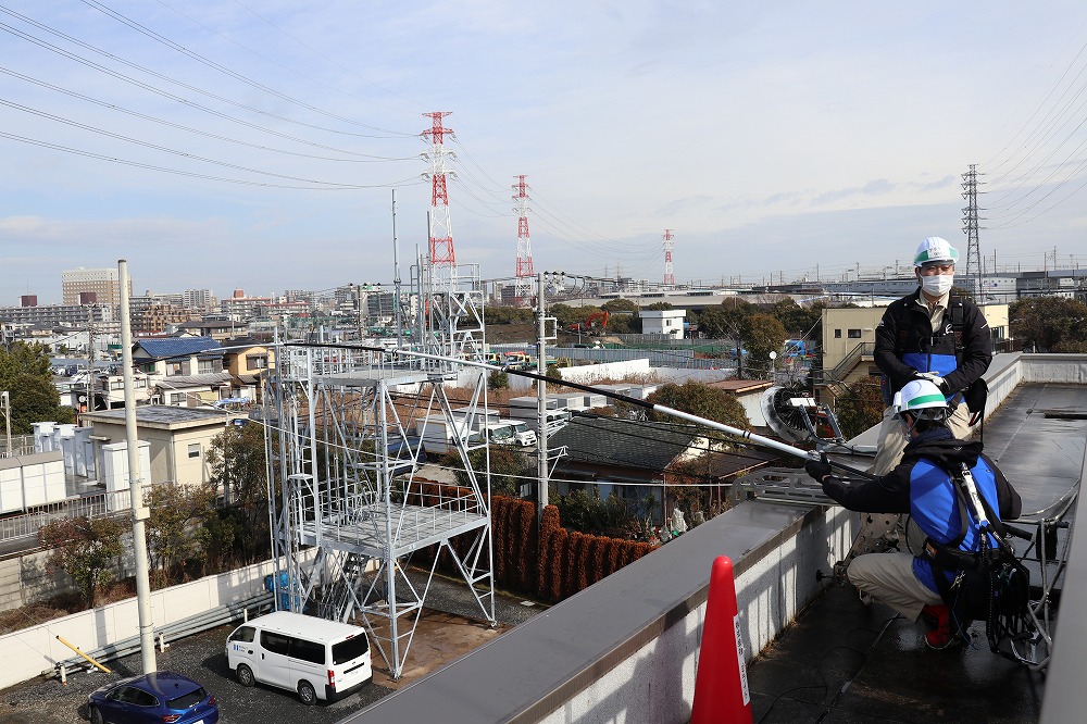 2点係留の際の建物屋上部の様子。釣りざお状のブラケットを設置し、外壁に沿ってひもを垂らして地上部で固定する。このひもをガイドにしてドローンが飛行するので経路から外れる危険性が低い（写真：日経クロステック）