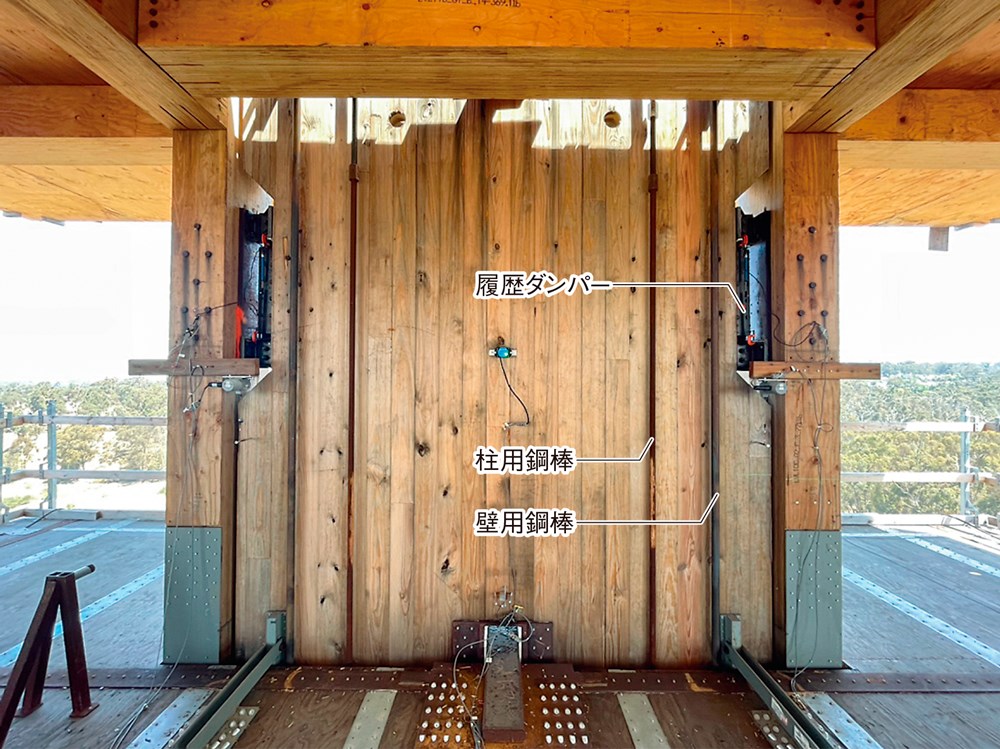 改修後の試験体の耐力壁。4本の鋼棒が見える。壁中央側の2本の細い鋼棒が柱用、壁外側の2本の太い鋼棒が壁用だ。壁用鋼棒2本の間隔はおよそ2m。柱と壁の間には履歴ダンパーを入れた（写真：住友林業の写真に日経クロステックが加筆）