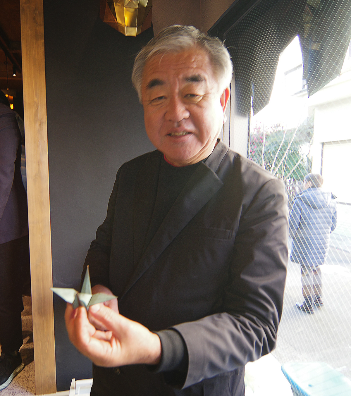 ウチノ板金がつくった板金の折り鶴を手に取る隈研吾氏（写真：日経クロステック）