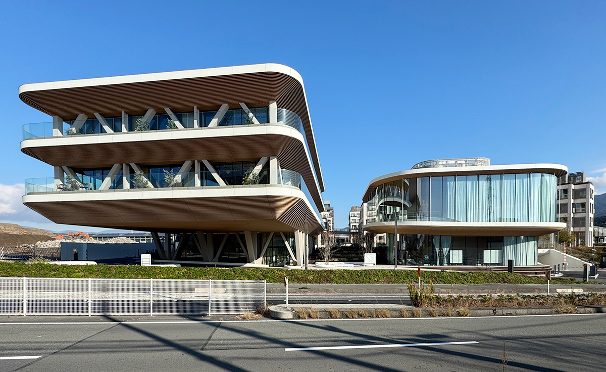実証都市「Toyota Woven City（トヨタ・ウーブン・シティ）」のメインアプローチ。左がオフィス棟で、右が「Woven Welcome Center」。建物は曲線的な外観（写真：日経クロステック）