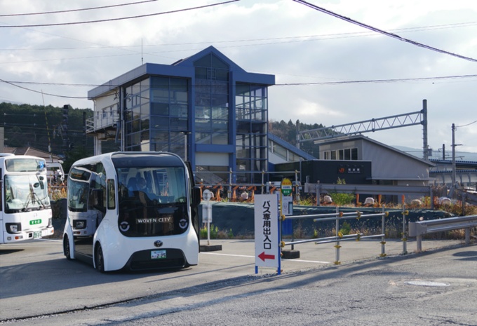 奥に見えるガラス張りの建物がJR御殿場線の岩波駅。手前に見える乗り物はトヨタの電気自動車「e-Palette(イーパレット)」。駅とウーブン・シティの間を往復運行している(写真:日経クロステック)
