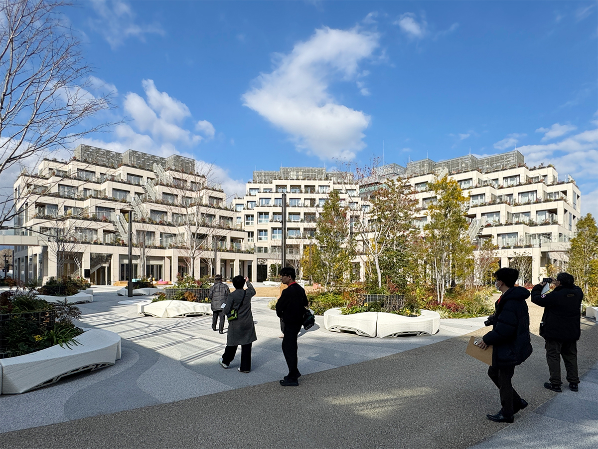 コートヤードを囲むように住居棟が立つ。植栽を囲う白いベンチは建設3Dプリンターで制作した（写真：日経クロステック）