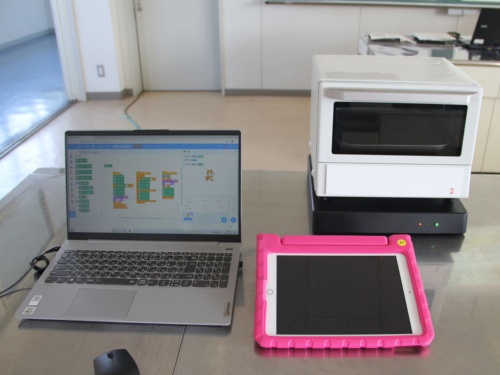 授業で使われた「Scratchトースター」（右上）とプログラム用のノートパソコン（左）、タブレット端末（右下）
