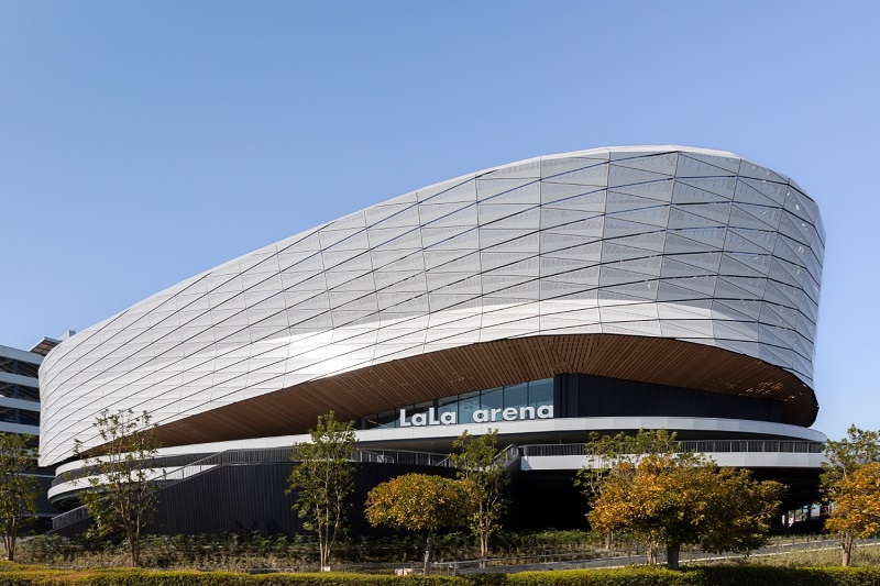 竣工直前の多目的アリーナ「LaLa arena TOKYO-BAY（ららアリーナ 東京ベイ）」。船の航跡とジェット気流をイメージした有孔アルミパネルの外観が特徴（写真：三井不動産、MIXI）
