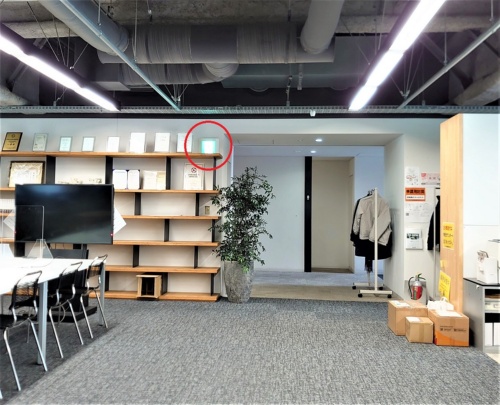 VR避難訓練の後、対象オフィスに連れて行ってもらった。職場がVR空間に忠実に再現されていたことが分かる。非常口誘導サイン（赤い丸印）もVRで見たままの位置にあった（写真：日経クロステック）