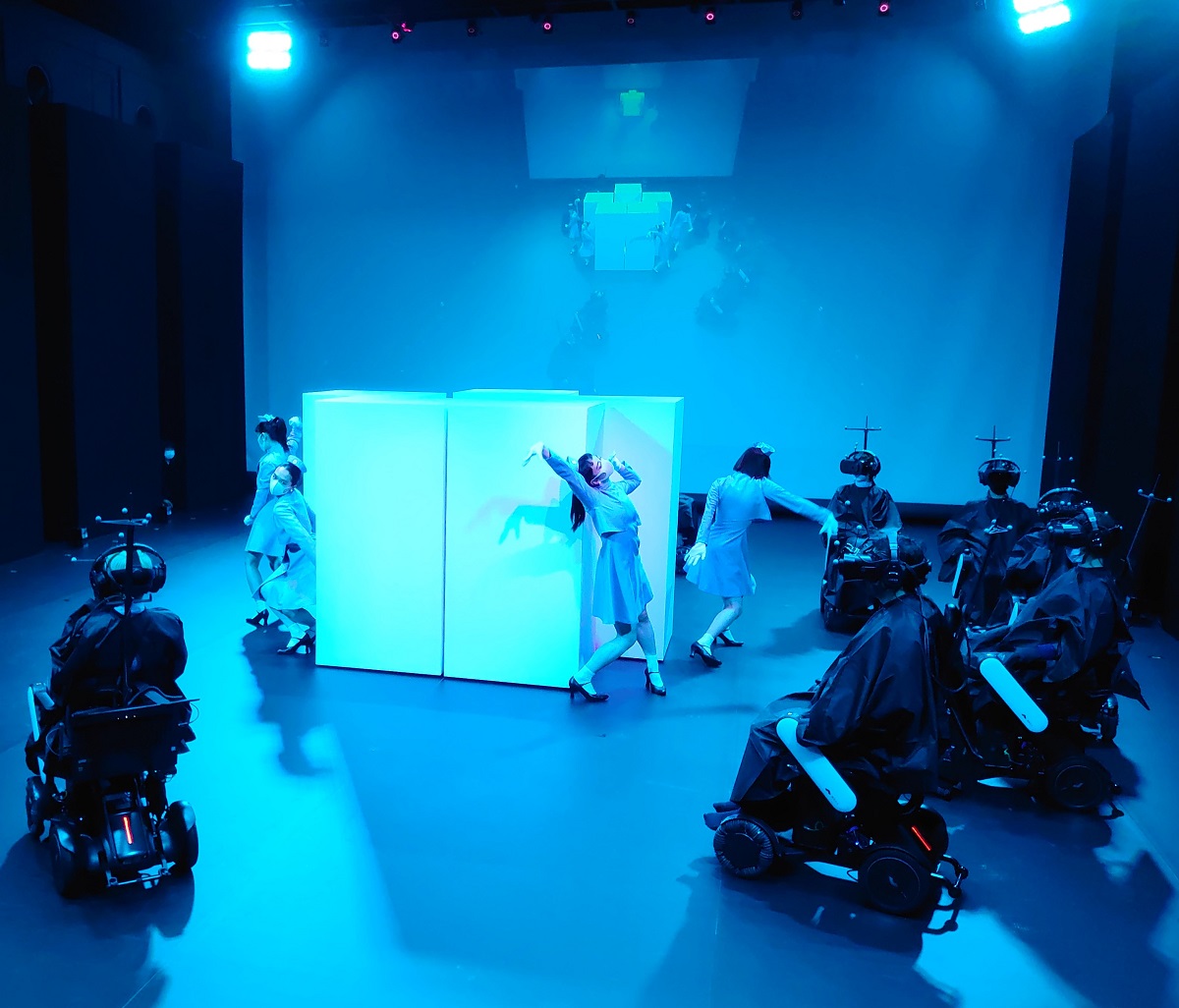 白いボックスの周りでダンサーが踊るシーン。写真のような客席からの眺めと、HMDで見ている世界は全く別物（写真：日経クロステック）