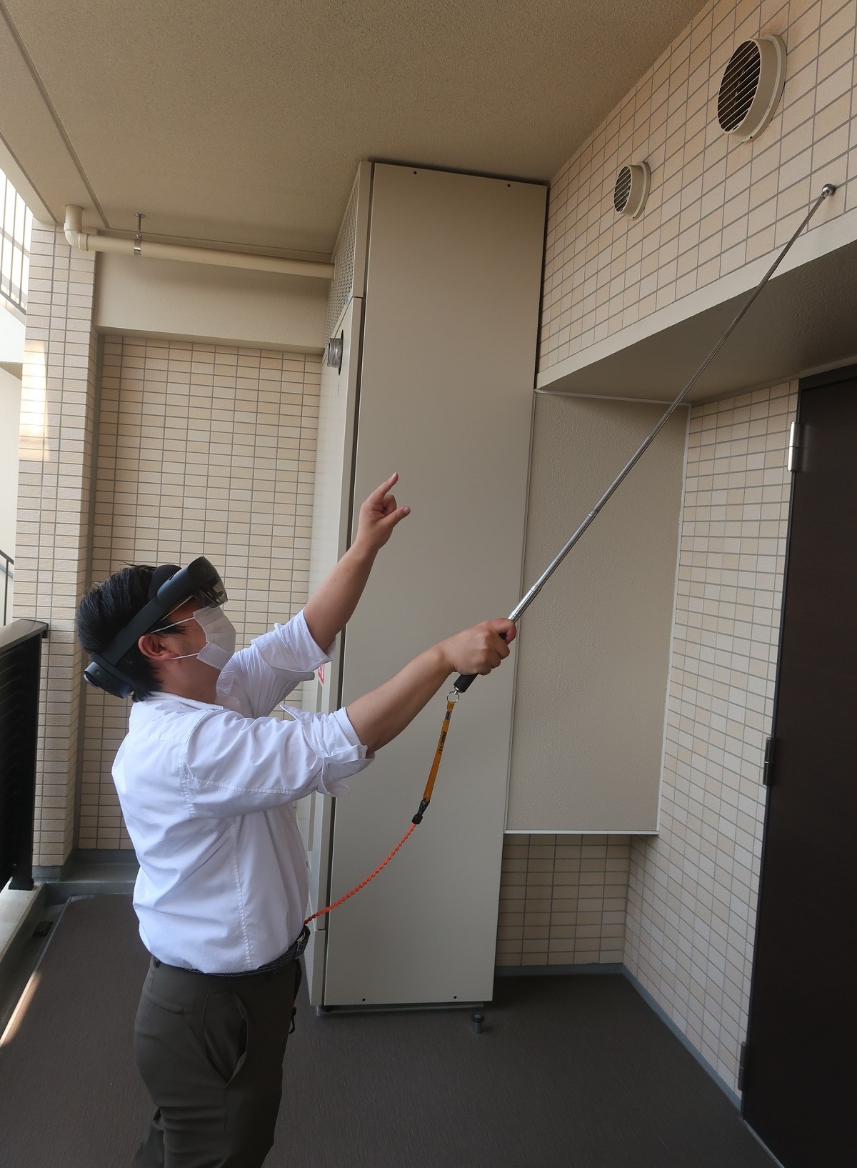 HoloLens 2をかぶり、タイル打診検査を体験している私。AR表示は指先で操作する。手に持っているのは、検査に使う「タイル打診棒」（写真：日経クロステック）