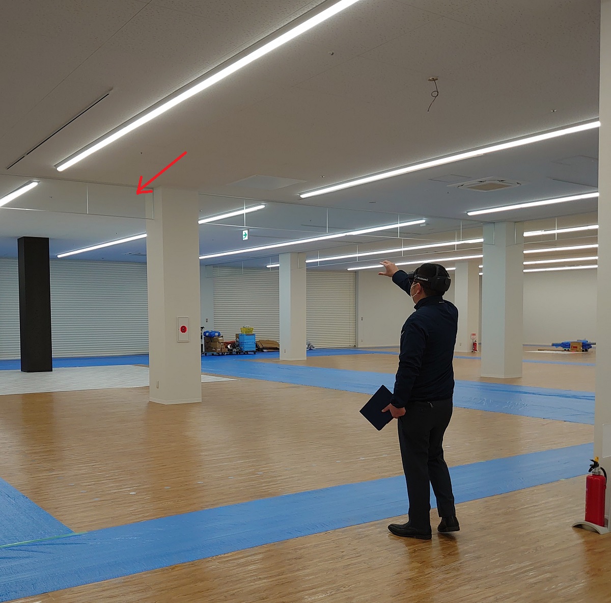 HoloLens 2をかぶり、天井の透明な垂れ壁（赤い矢印）に近づいていく日本ERIの検査担当者（写真：日経クロステック）