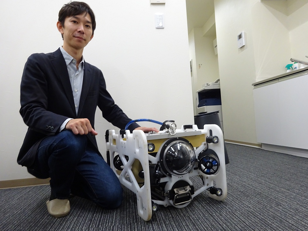 フルデプスの伊藤昌平社長と、水中ドローンの「DiveUnit300」。もともと「深海魚とロボットが好き」という伊藤社長の趣味が高じて開発を始めた。大学在学中から試作機の開発に従事し、2014年に会社設立。初めて造った水中ドローンは深さ1000mまでの潜水に成功した（写真：日経コンストラクション）