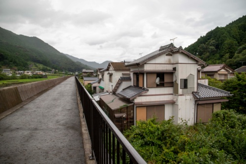 高岡地区にある輪中堤の管理用通路の上に立って上流側を眺めたところ。左側のパラペットの向こう側は相野谷川。右側の住宅は2011年の洪水で被災したときの状態のまま。人が住んでいる様子がない建物が大部分となっている。2020年7月27日撮影(写真:水源地環境センター)