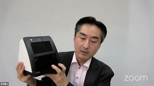 顔認証付きカードリーダーを提示して説明する大竹雄二室長