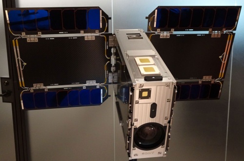 開発した人工衛星のモックアップ。サイズは6U（33cm×20cm×10cm）。同社製のズームレンズ付き4Kカメラを内蔵する。民生品だが、耐熱性や真空対応など宇宙仕様にカスタマイズしているという。