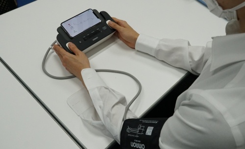 心電計付き血圧計で測定している様子。機器の上にスマホを設置して使う。1分ほどで血圧と心電図が記録された。