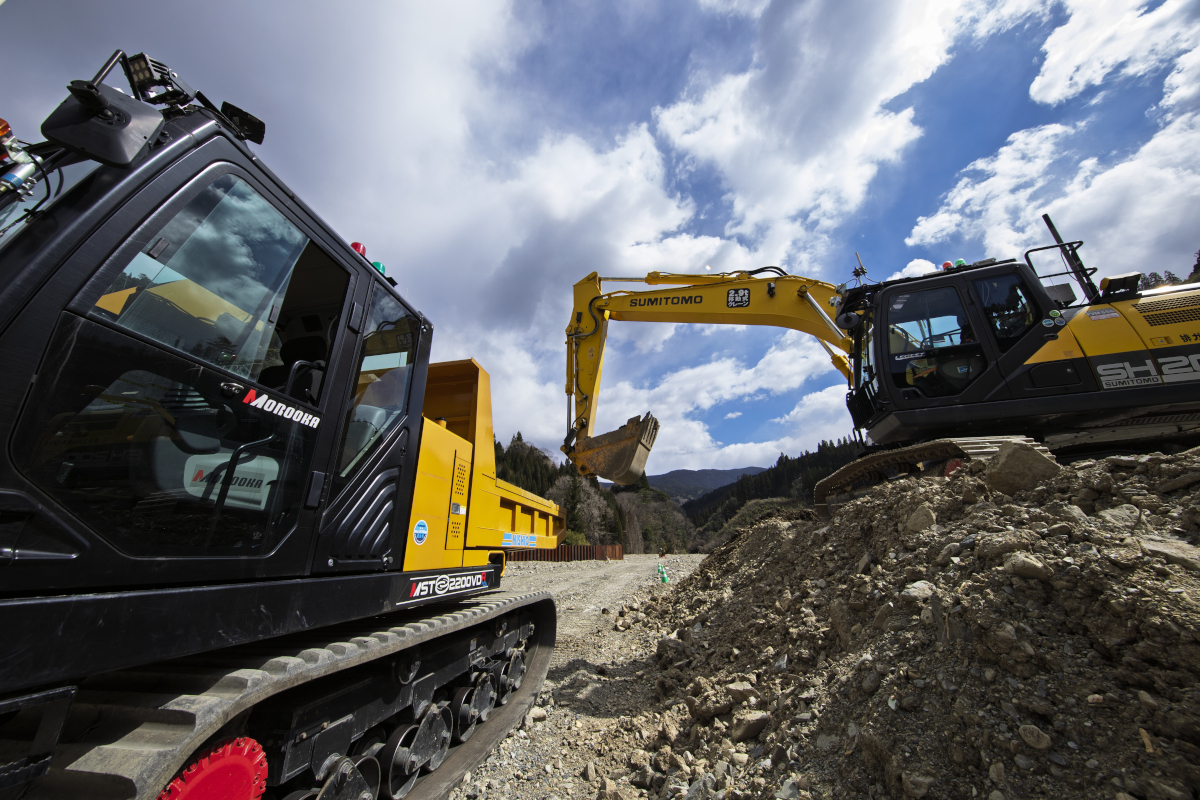 宮崎県椎葉村の工事現場で稼働する2台の建設機械。オペレーターは乗っていな い。右側にあるバックホーは遠隔地で操作しており、土砂の積み込みが終わると左側のクローラーダンプが自律搬送する（写真：イクマ サトシ）