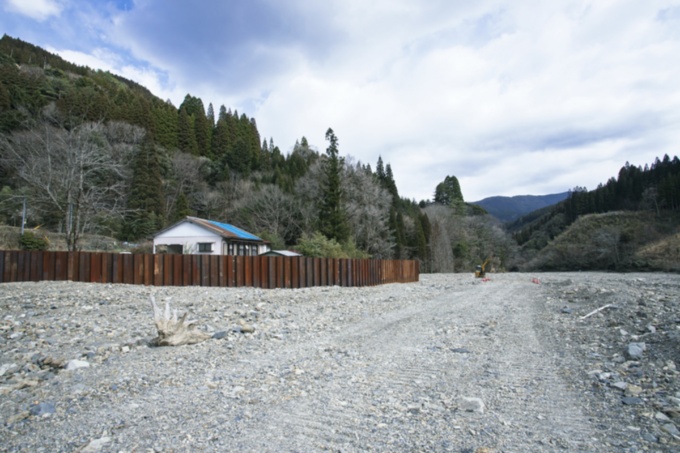 現場周辺にある人家。もともと斜面沿いに立っていたが、上流からの土砂で平地になり、現在は囲いで覆われている(写真:イクマ サトシ)