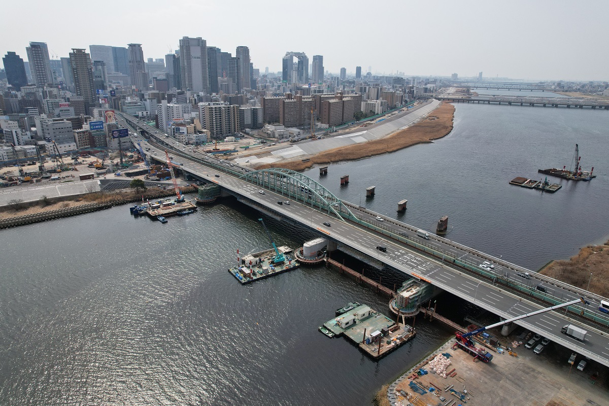 上空から現場を眺める。淀川に立つ3本の橋脚に近接する供用中の道路は、国道423号。写真奥の左岸川の河川敷で工事を進めているのが、淀川左岸線２期だ（写真：生田 将人）