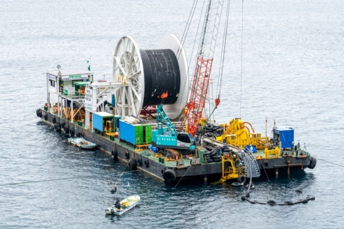 送水管を敷設する台船。黒いブイで浮かべた送水管をドラムから伸ばしている(写真:大村 拓也)