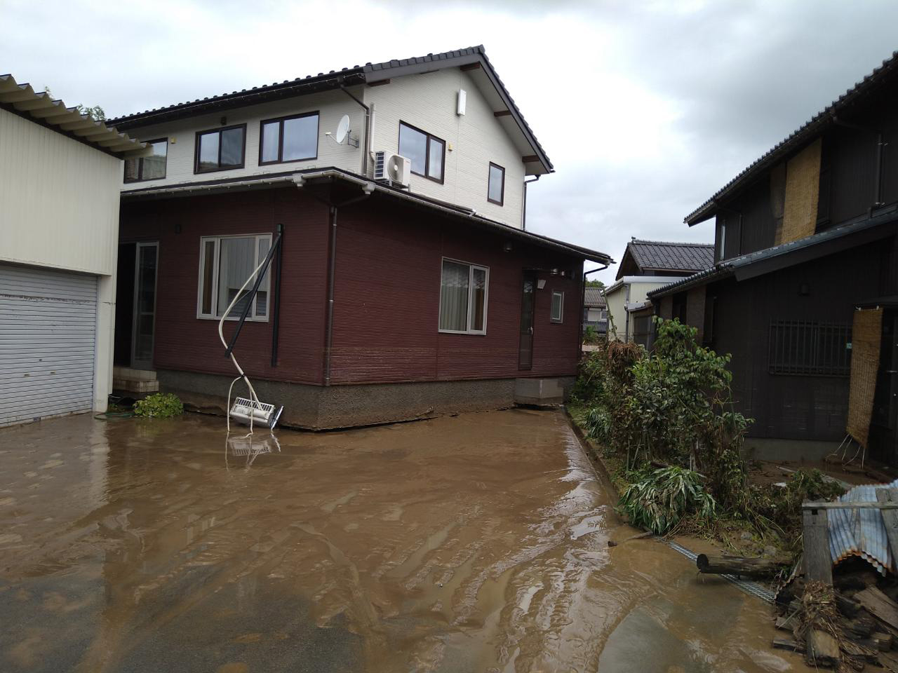 水が引いた後の住宅の様子を南側から見る。時計回りに回転して、西側の車庫にぶつかる寸前だった。外壁に取り付けていたエアコンの室外機が基礎の下に挟まれた状態で、建物が着地していた。住宅は延べ面積が約143m<sup>2</sup>、建築面積が約93m<sup>2</sup>の2階建てだ（写真：住民提供）