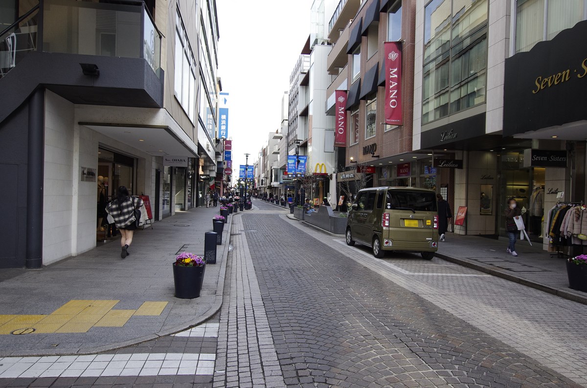横浜元町ショッピングストリートのメイン通りは延長約600m。車道幅員を縮小・蛇行させて走行車両の速度低下を促し、歩車共存空間を生み出す「ボンエルフ型」の導入で、全国でも早かった整備例の1つだ。この整備手法では、千葉県浦安市の団地「入船西エステート」（敷地内道路）や松江市の南殿町商店街などでの導入例もよく知られている。（写真：下田 健太郎）