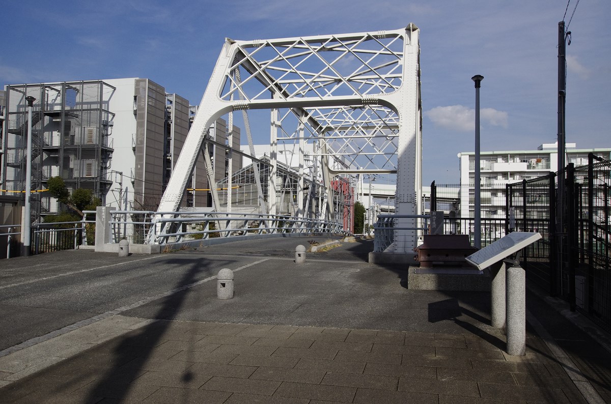 新山下運河に架かる霞橋は支間長31.4mの小ぶりな橋で、橋上は片側歩道と新山下1丁目交差点方向に一方通行の1車線道。明治時代に生まれた英国製プラットトラス橋の部材を再利用し、2回にわたる移設を経て現役を続ける「幸運な橋」だ。横浜市が旧橋の架け替え事業として発注し、設計はオリエンタルコンサルタンツが担当した。（写真：下田 健太郎）