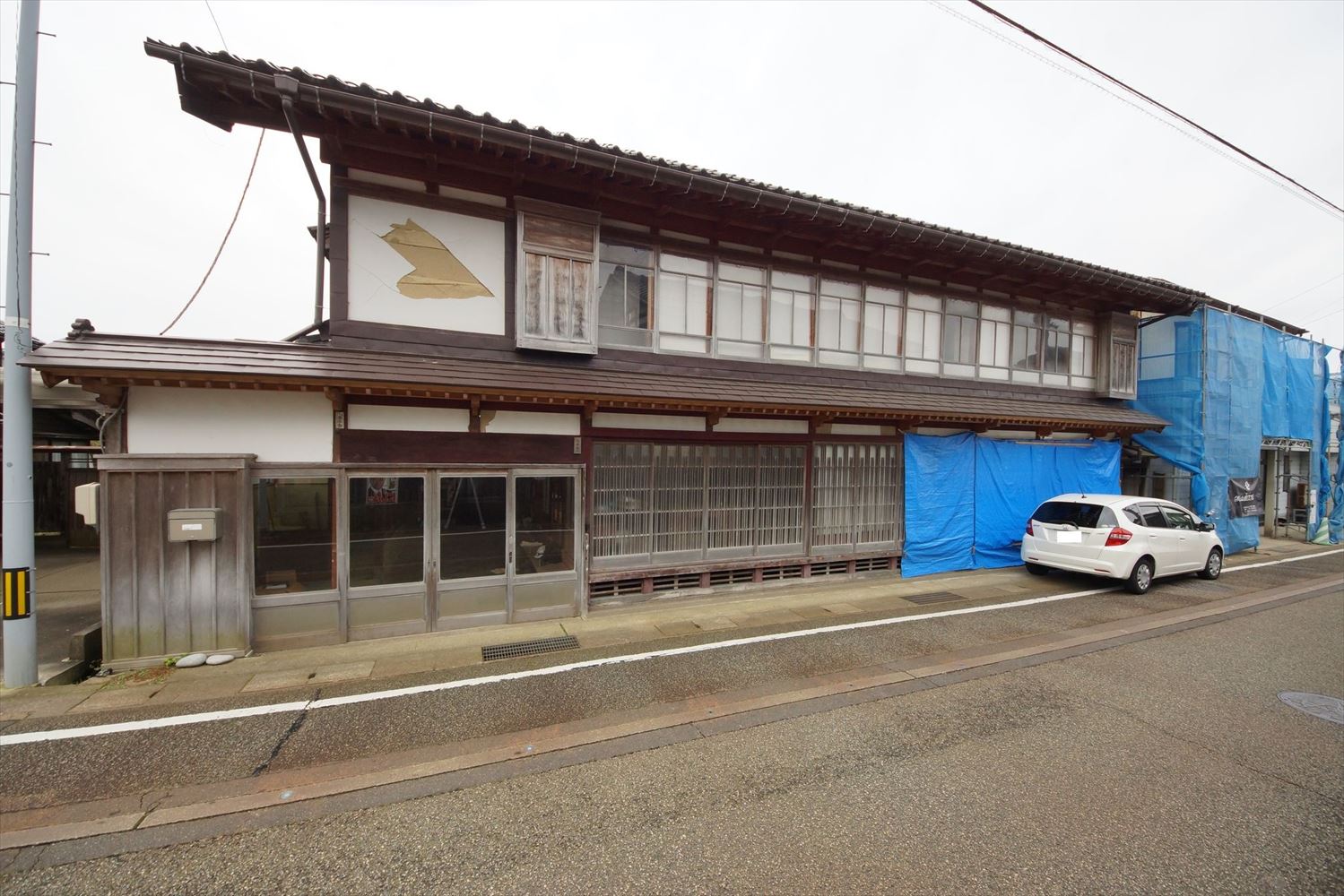 珠洲市正院町に立つ大正時代に建てられたと推定される間口の広い住宅の、23年奥能登地震後の状態。柱が一部折れて梁間（はりま）方向の建具が大破していた。道路側にほとんど壁がなく、和室が6つ設けられている。土台足固めなどの床下装置にも損傷や劣化が生じていたので、地震で壊れやすい状態だった。住人は改修するか取り壊すかを悩んでいた（写真：建物修復支援ネットワーク）
