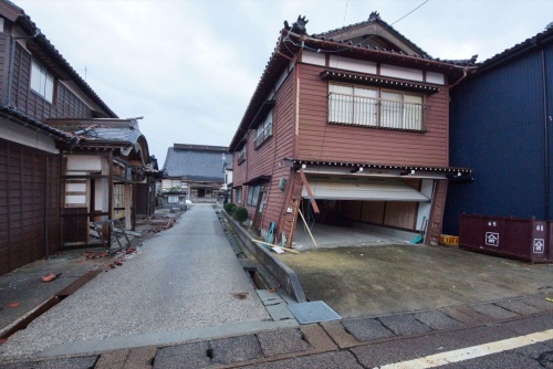同住宅の24年能登半島地震後の状態。耐震補強工事の一部が完了していた。1階の車庫が西側に傾き、くの字に変形したが、左側の参道への倒壊を免れた。門型の開口部に添え柱を追加し、基礎を補強する工事を予定していたが、実施前に能登半島地震後が発生してしまった(写真:建物修復支援ネットワーク)