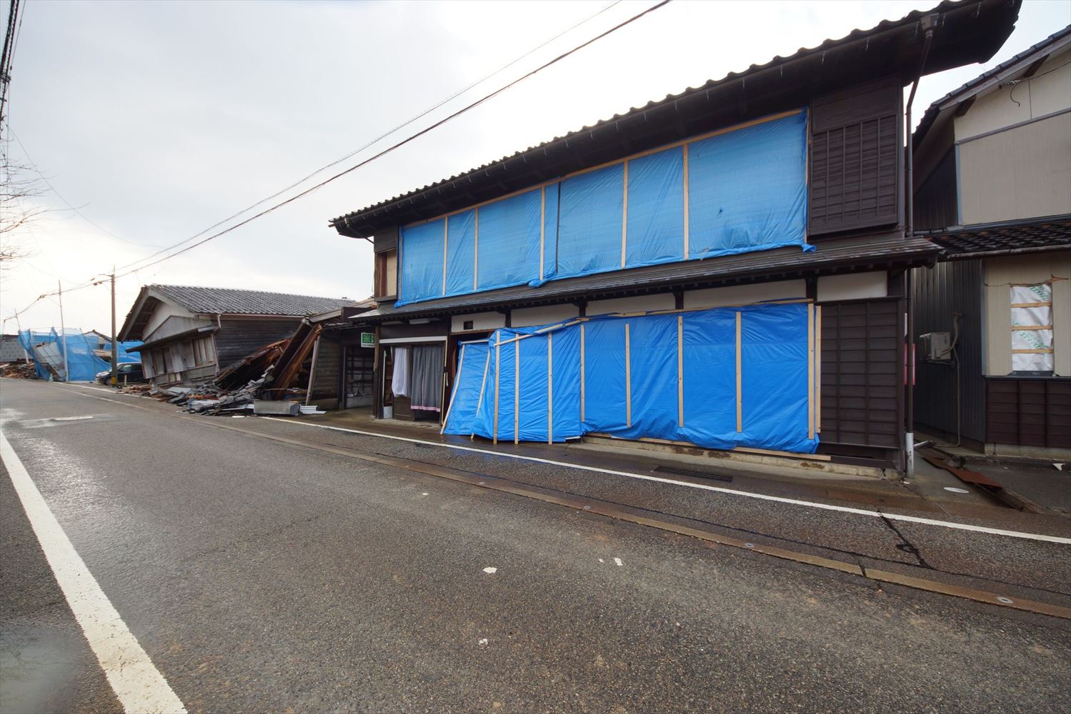 同住宅の24年能登半島地震後の状態。奥能登地震後に張っていた合板が一部脱落した。一部の柱と土台接合部が離れて、コーチボルトで留めていた筋交いは抜けたが、大きな滑りや変形は生じていなかった。奥能登地震では残っていた左隣の家は、層崩壊した（写真：建物修復支援ネットワーク） 　