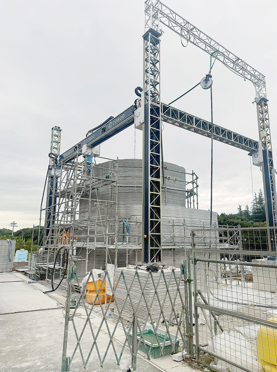 地上2階建ての3Dプリンター住宅「Stealth House」の2階外壁部分を印刷している様子。デンマークに本社があるCOBOD Internationalの大型建設3Dプリンターを購入して利用した。材料はタイの建材メーカーであるSCG（Siam Cement Group）が開発した3Dプリント用のモルタルを採用。日本の気候に合わせて配合を調整した（写真：オノコム）