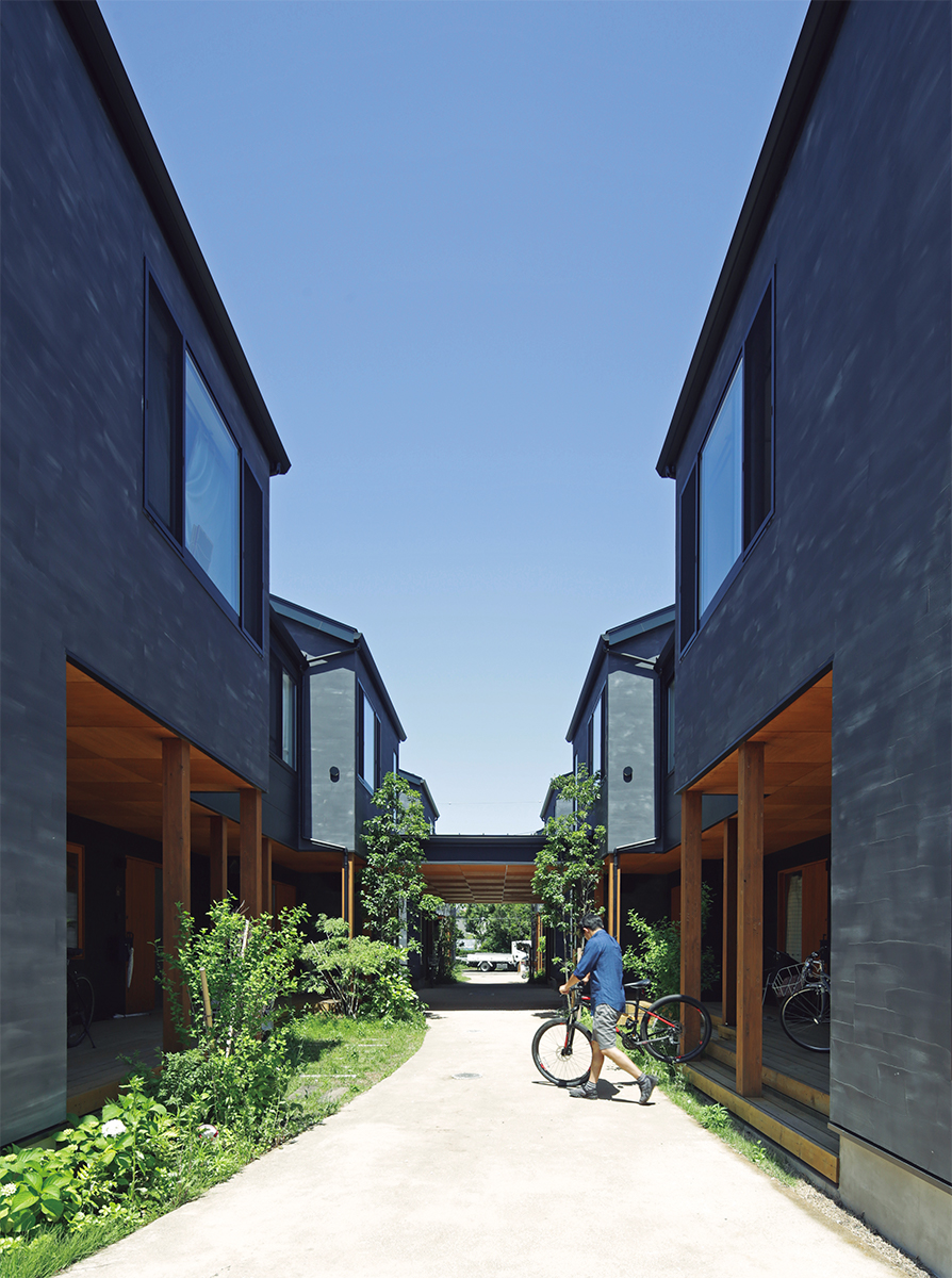 住棟の真ん中を路地が貫き、一部は屋根付きの広場のようになっている。路地の両側にウッドデッキのポーチ、その奥に各住戸の玄関がある。写真は13戸が入る1期の「椚（くぬぎ）棟」。2017年10月に完成した（写真：安川 千秋）