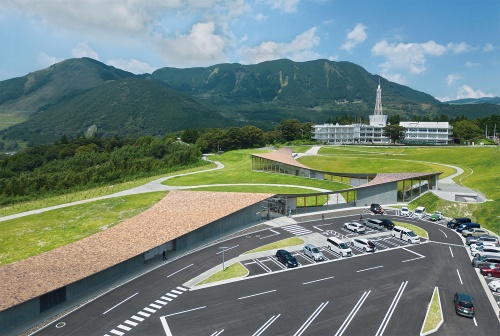 ドローンで撮影した施設の全景。奥の震災遺構を目指す道のように曲がりくねった屋根が続く。広大な敷地を駐車場と2つの芝生スペースに区切る配置計画だ(写真:イクマサトシ)