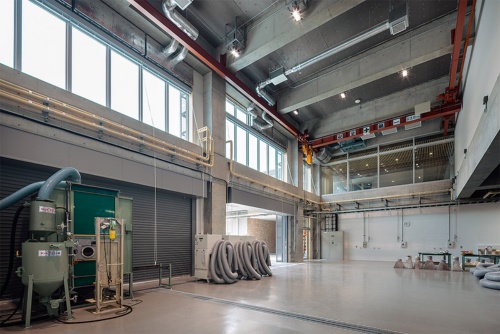 4号館1階の共通工房「石材加工機械室」の内部。奥2階に「アートコモンズ大学院」が見える(写真:吉田 誠)