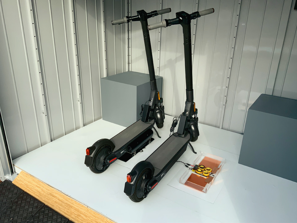 写真1■ 電動キックスケーターを充電スポットに止めると自動で無線充電が始まる。右のキックスケーターにつながっているのは受電機器の模型（写真：大成建設）