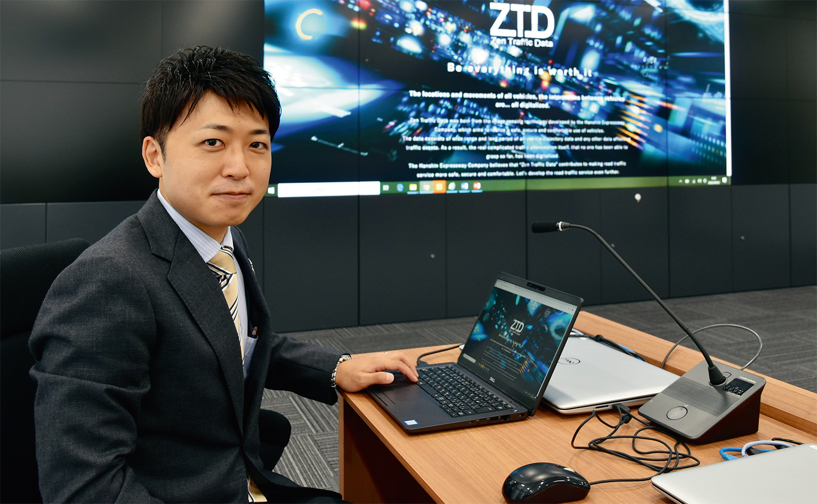 写真1■ 阪神高速道路会社の石原雅晃氏。右奥はZTDプロジェクトのイメージ画像（写真：日経コンストラクション） 