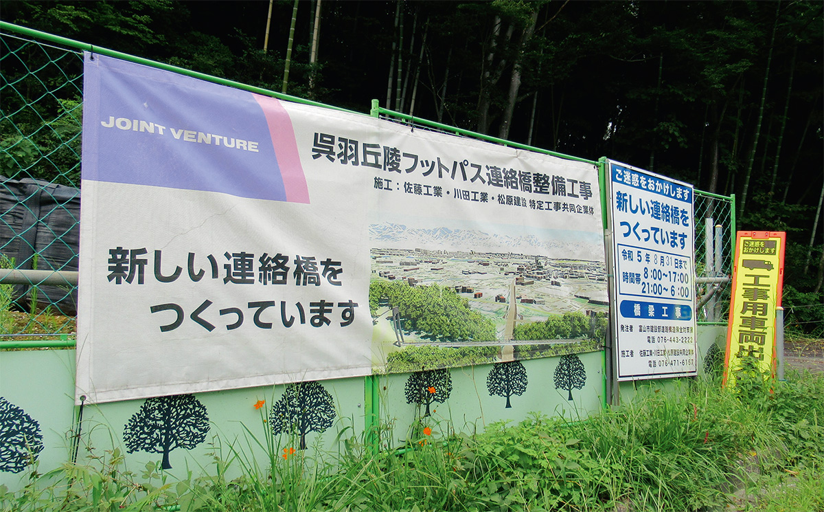資料1■ 呉羽丘陵フットパス連絡橋の施工現場にある掲示。呉羽丘陵を分断する県道44号に長さ約124mの人道橋を架ける。施工者は佐藤工業・川田工業・松原建設JV（写真：日経クロステック）
